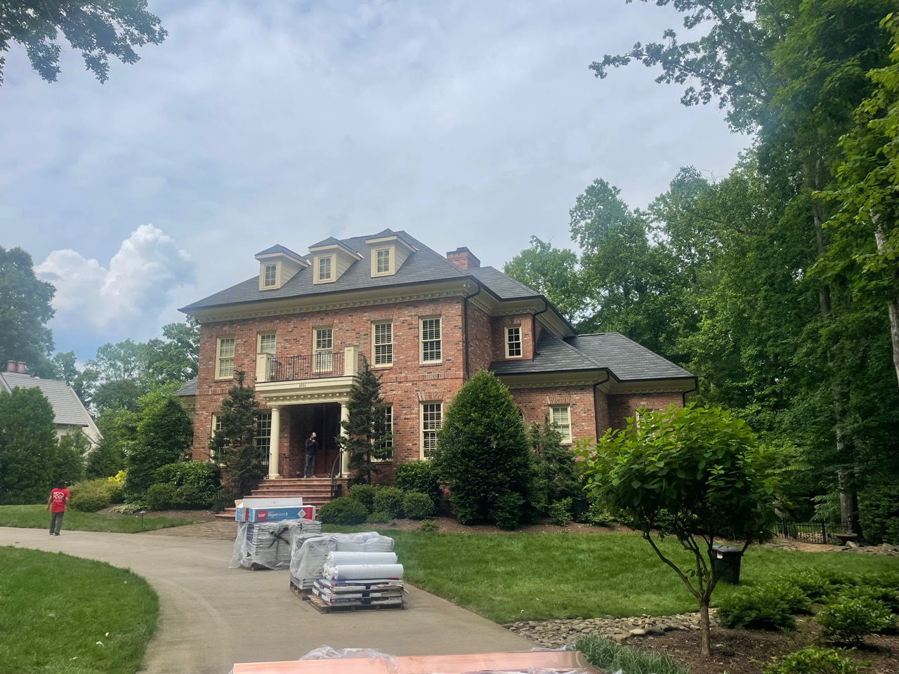 Roofing materials staged in the driveway of a large brick estate during an active residential roofing project