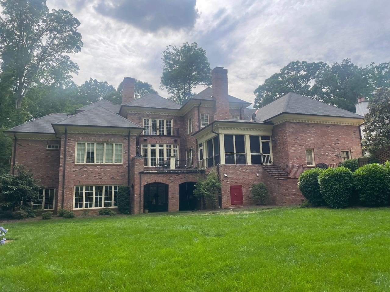 Rear ground-level view of a dark architectural shingle roof across multiple wings of a large brick residence