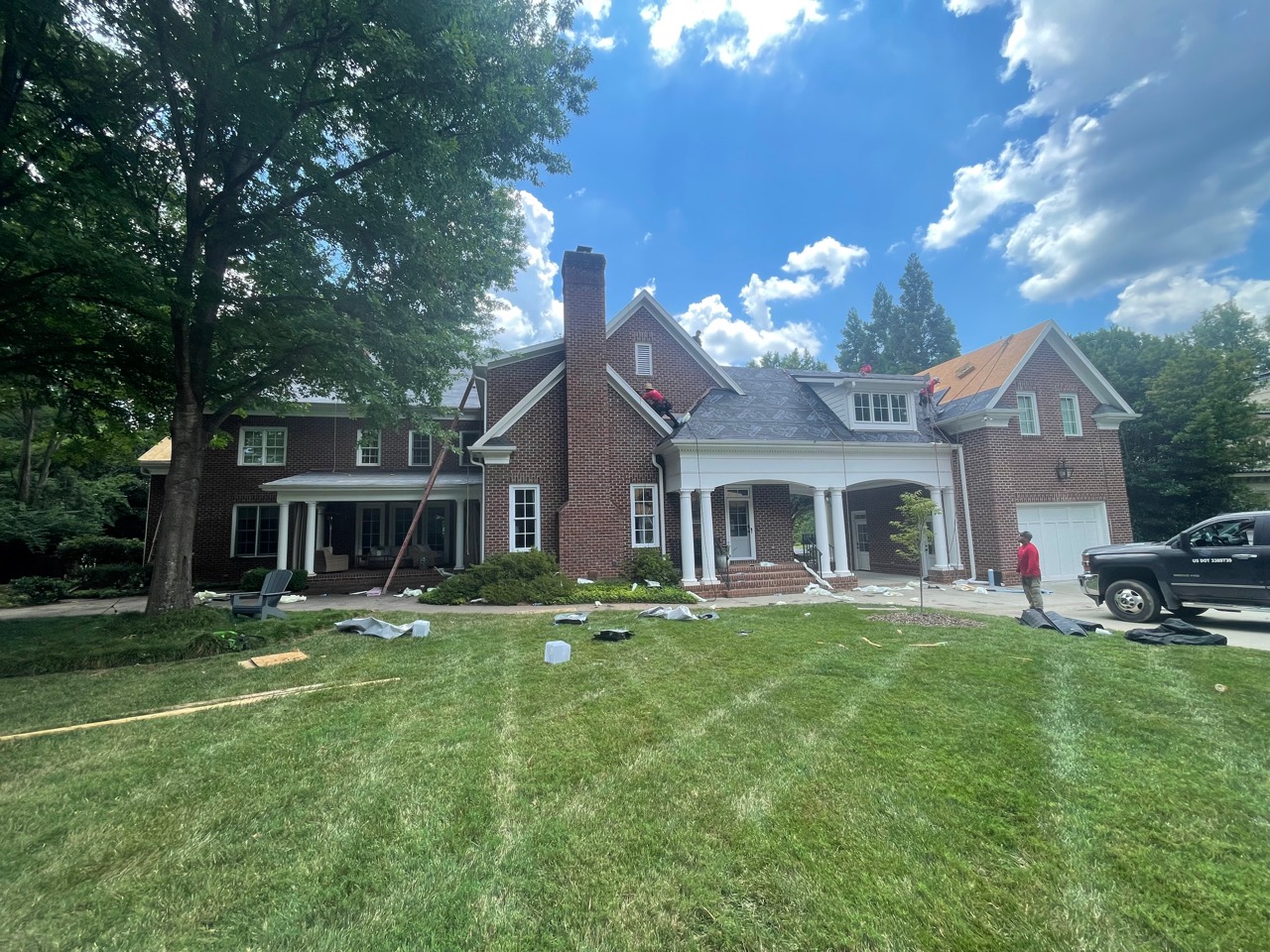 Ground-level view of roofing underlayment and installation work across connected sections of a large brick estate