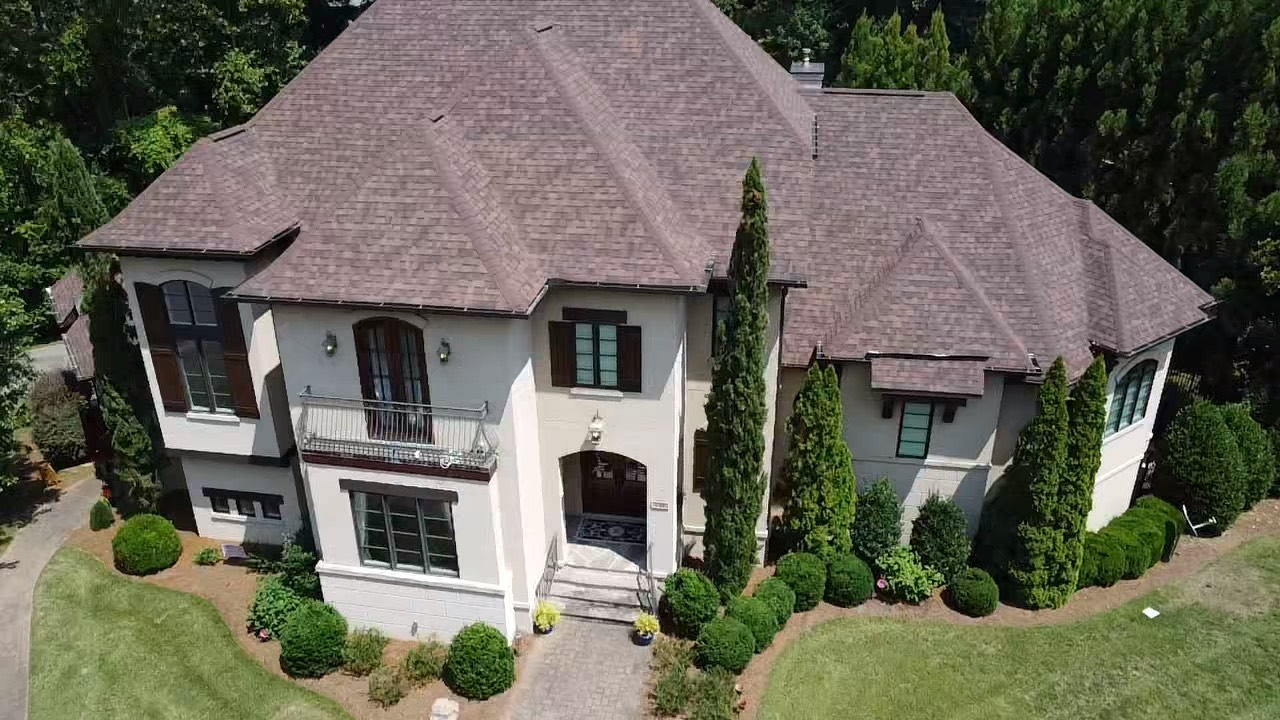 Front aerial view of a warm brown architectural shingle roof on a large stucco residence