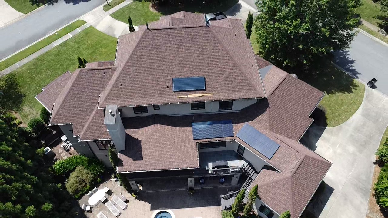 Top-down aerial view of a brown shingle roof with integrated solar features on a large residence
