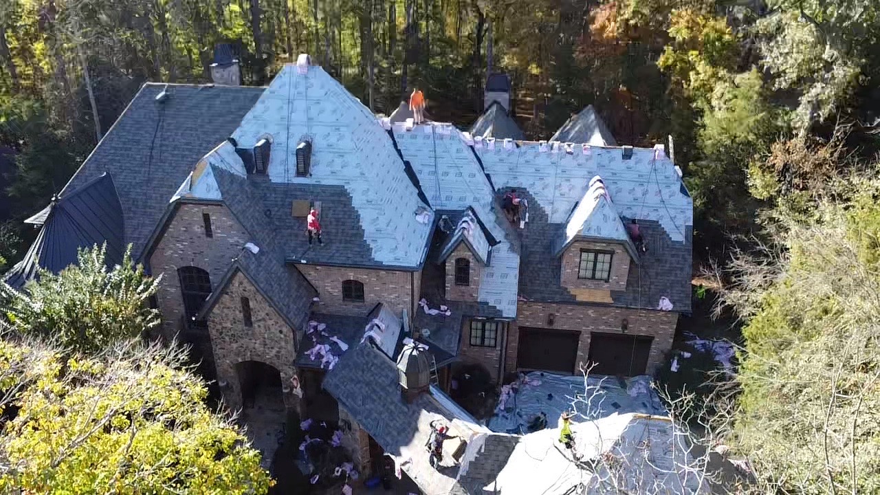 Aerial view of shingle installation in progress across a complex brick estate roof