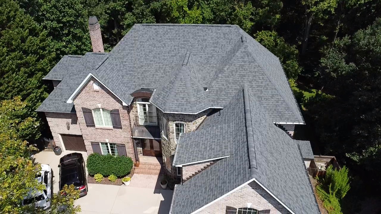 Front aerial view of gray architectural shingles on a large brick and stone residence