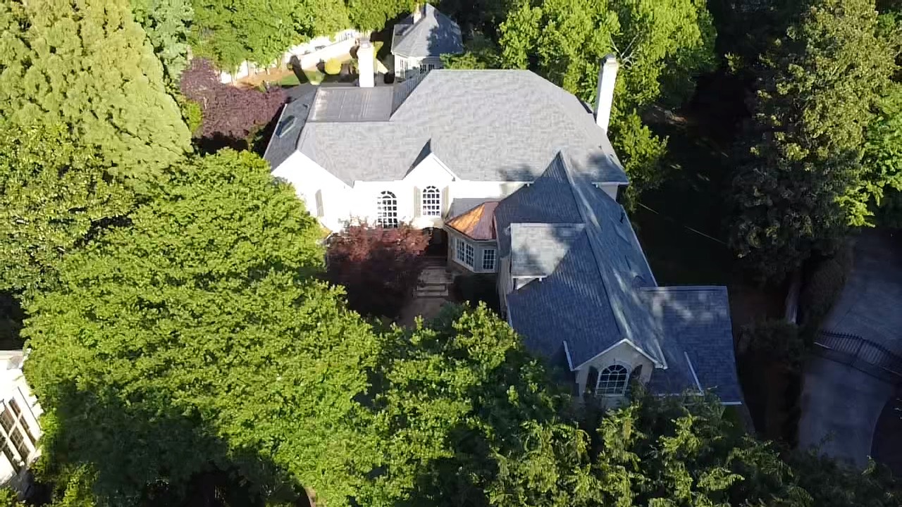 Aerial view of a gray shingle roof with a copper bay-window roof on a wooded residential property