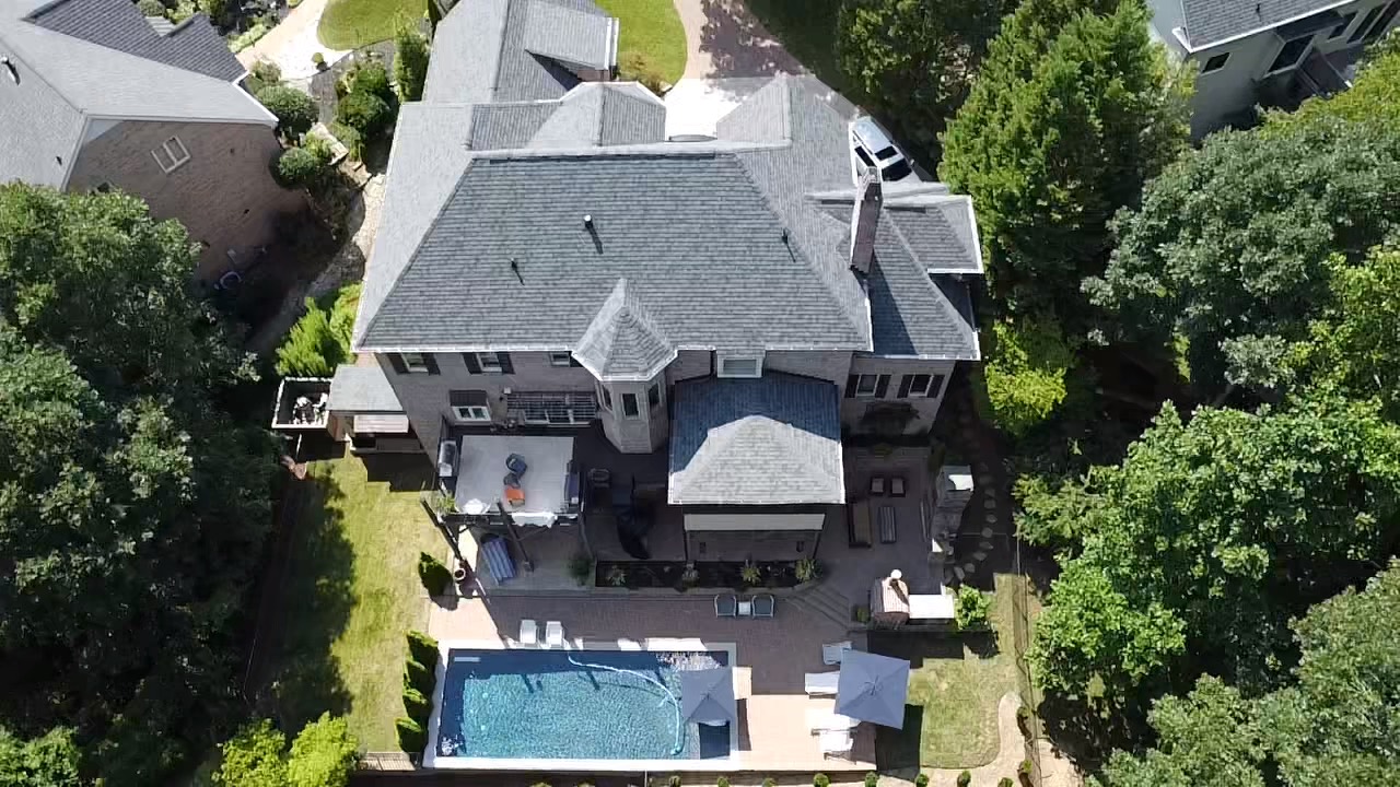 Top-down aerial view of a gray shingle roof on a residence with a pool and outdoor living areas
