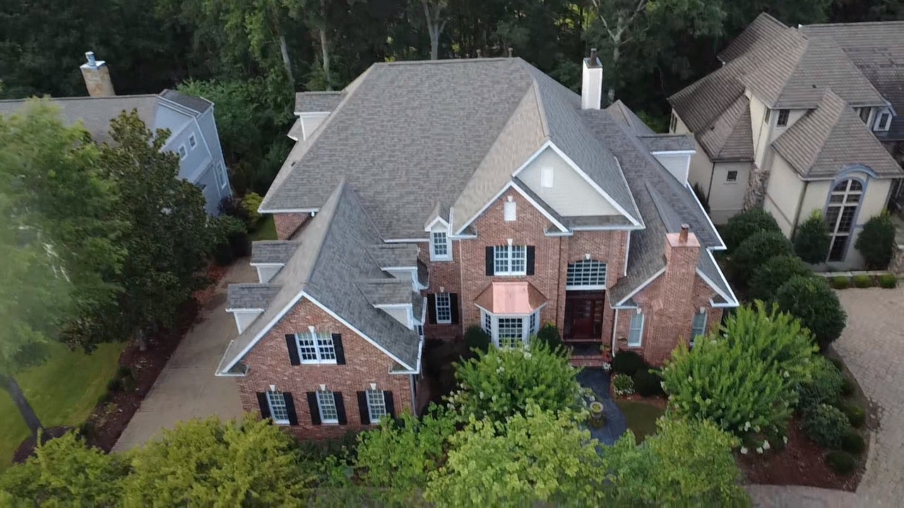 Aerial view of layered architectural shingle rooflines on a large brick residence