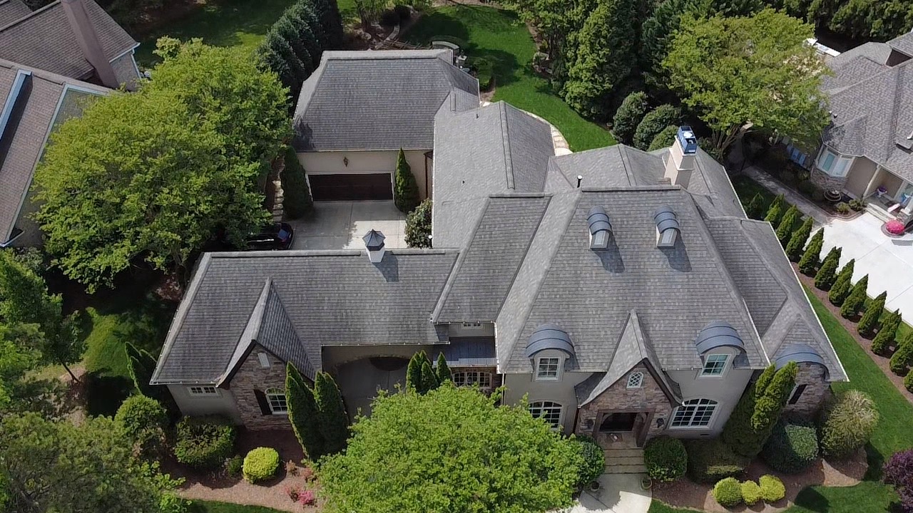 Aerial view of a luxury residence with architectural shingles, multiple rooflines, and curved dormers