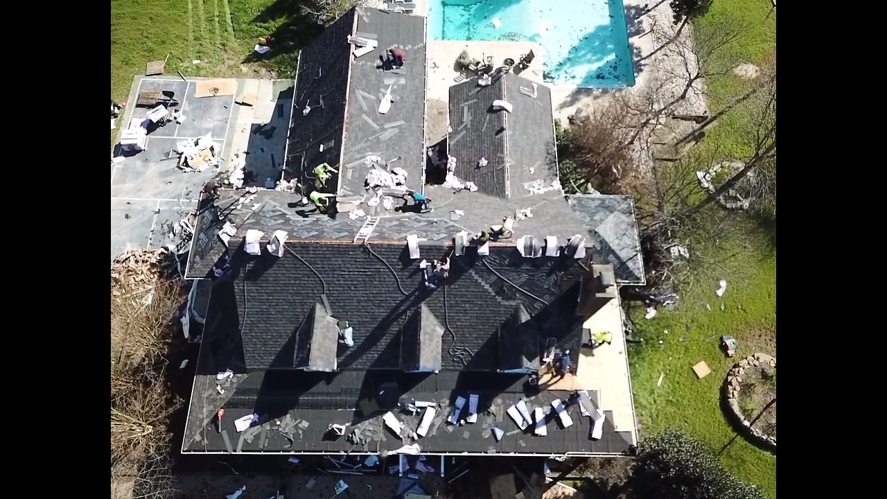 Top-down aerial view of a residential roof replacement in progress with crews working across multiple sections