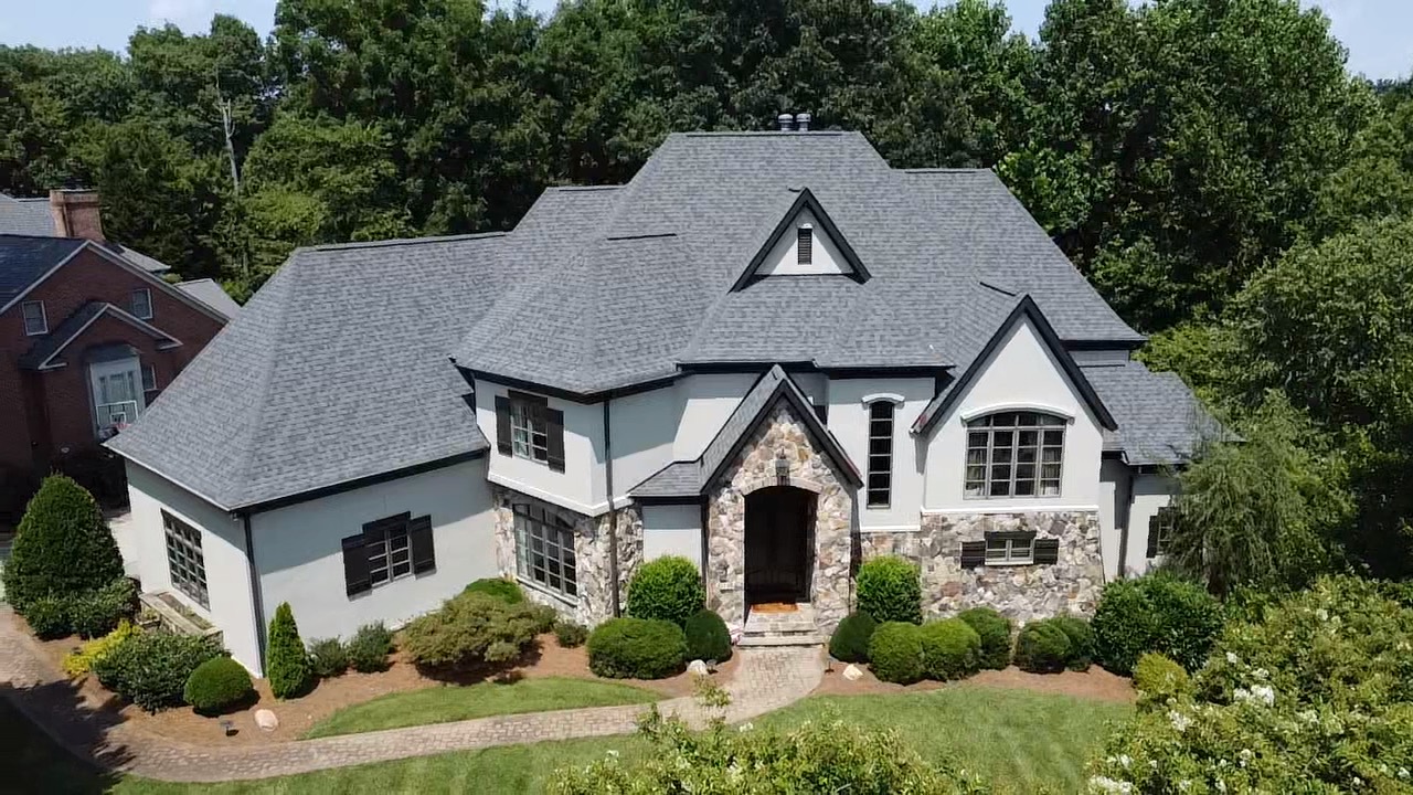 Front aerial view of a gray architectural shingle roof on a white and stone luxury residence